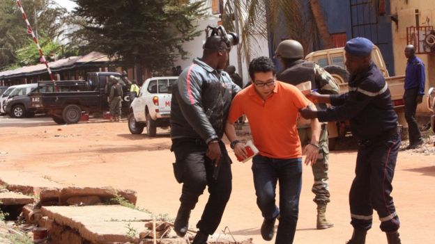 Mali troops assist a hostage, centre, to leave the scene of the hotel