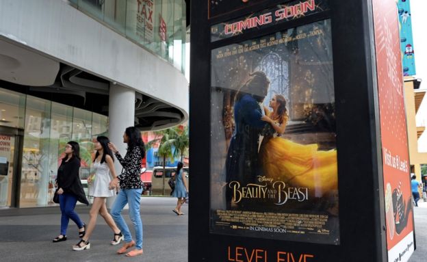 People walk past a poster for the film Beauty and the Beast in Singapore on 14 March 2017.