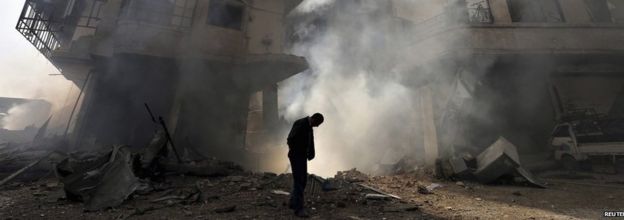 A man (with head bowed) walks in front of a burning building after a Syrian air force strike in Ain Tarma neighbourhood of Damascus January 27 2013