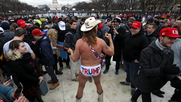 A cowboy dressed in underwear plays guitar as people gather on the National Mall.