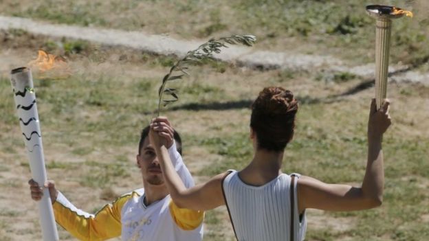 Greek actress Katerina Lehou, playing the role of High Priestess, passes the Olympic flame to the first torch bearer, Greek gymnast Eleftherios Petrounias (21 April 2016)