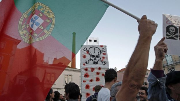 People protest with a Portuguese flag and a giant pen, representing the state budget delivered to the parliament, in front of the Parliament in Lisbon in October 2012.