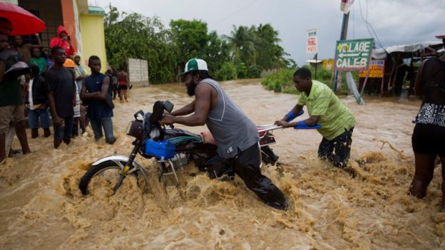 Men push a motorbike through a street flooded