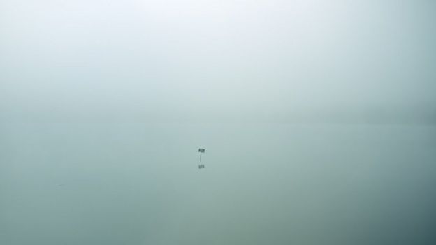 Un pequeño cartelito en la distancia en medio de un lago brumoso
