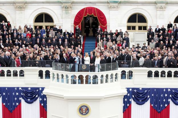 A photo from a distance captures Mr Trump raising his hand as he takes the oath of office as his family and various officials and dignitaries look on