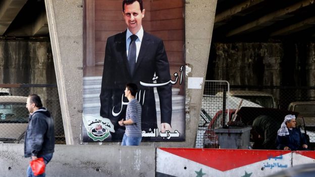 Syrian men walk past a poster bearing a portrait of President Bashar al-Assad in Damascus