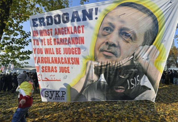 Протестующий в немецком Кельне несет баннер с изображением президента Эрдогана, скрывающегося под маской боевика ИГ