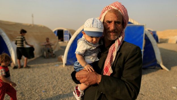 A displaced man carries his nephew as he stands beside tents upon his arrival at al-Khazar camp, east of Mosul, (26 October 2016)