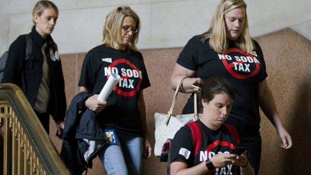 Women wearing 'no soda tax' T-shirts walk down the stairs looking glum