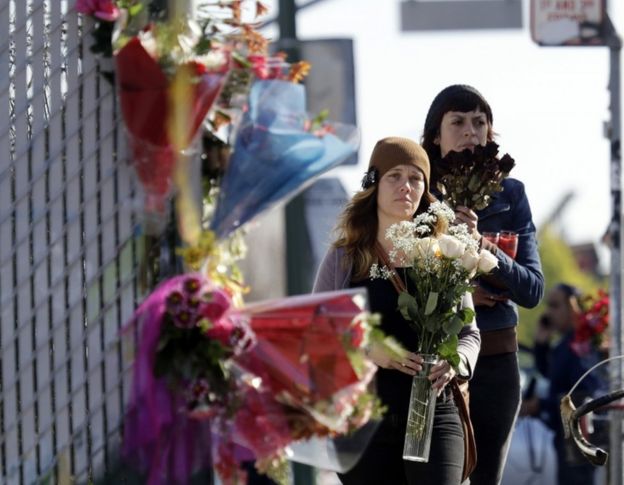 Well-wishers walk to place flowers at the scene in the aftermath of a warehouse fire, Sunday, Dec. 4, 2016, in Oakland, Calif.