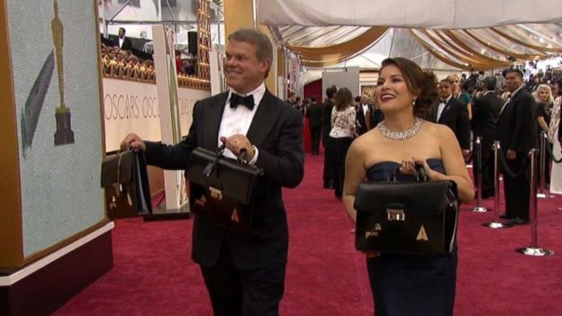 Martha Ruiz y Brian Cullinan, en la alfombra roja, con las maletas en las que cargan los sobres con los nombres de los ganadores.
