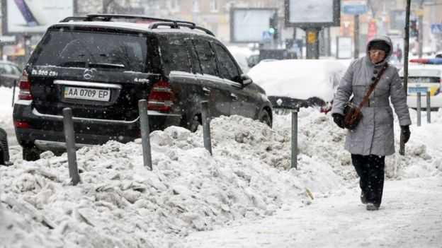 A woman walks past a snow dump along a road in Kiev, Ukraine. Photo: 9 January 2017