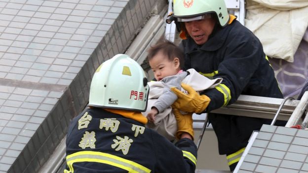 Rescue workers remove a baby from the site where a 17-storey apartment building collapsed after an earthquake hit Tainan