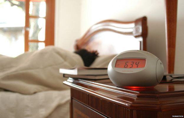 Person in bed, alarm clock on table