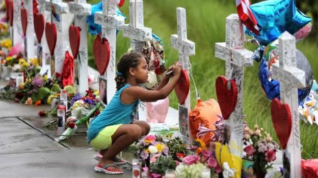 Seven-year-old Mekiha Thomas of Orlando signs one of the 49 crosses at a makeshift memorial outside Orlando Regional Medical Center (19 June 2016)