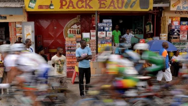 Bystanders look on as the pack of Cyclists competing in 150km cycling final in the the 11th Africa Games ride through an urban area on September 13, 2015