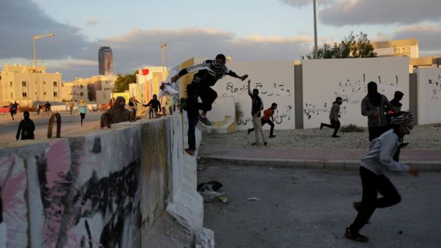 Bahraini protesters jump a cement barricade as police approach near the end of a march denouncing the execution of Saudi Shiite cleric Sheikh Nimr al-Nimr, on Sunday, 3 January 2016, in Daih, Bahrain