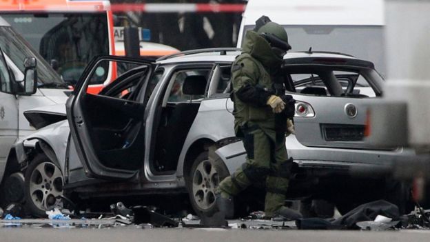 A bomb disposal specialist in protective gear passes by an exploded car as he investigates the site of the blast in Berlin, eastern Germany, Tuesday, March 15, 2016