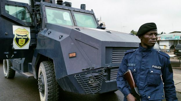 policeman with a gun stands in front of anti-riot vehicle
