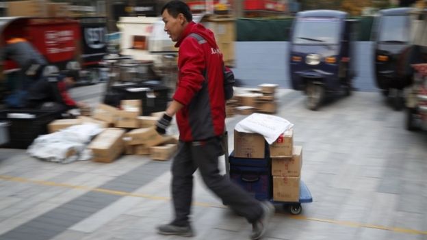 A delivery worker pulls a cart loaded with goods past workers sorting parcels for their customers in Beijing
