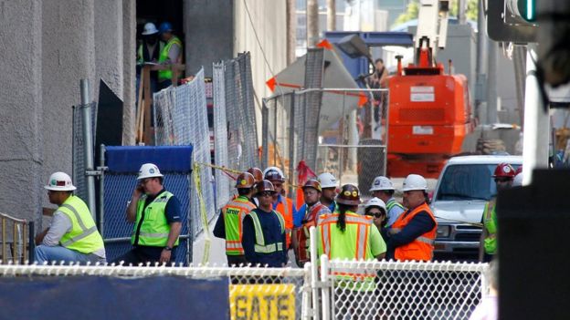 Construction workers gather at the base of the Wilshire Grand Tower on South Figueroa Street where a worker fell to his death