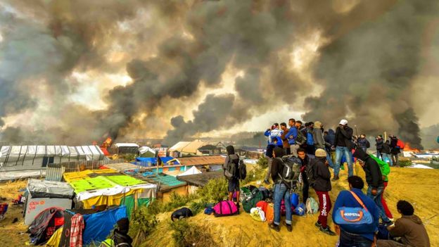 مهاجرون يتطلعون الى النيران وهي تلتهم مخيم الغابة في كاليه