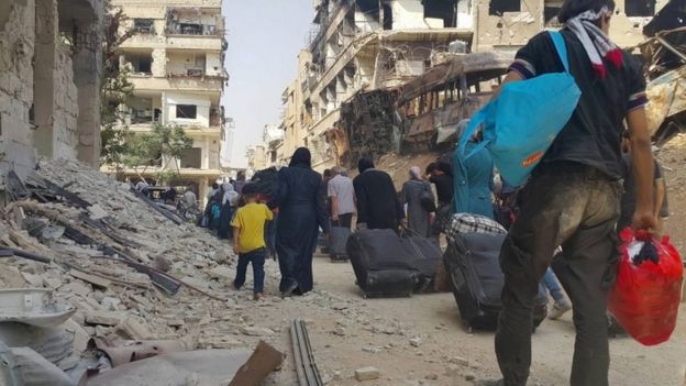 Residents of Darayya, in Syria, carry belongings as they prepare to evacuate