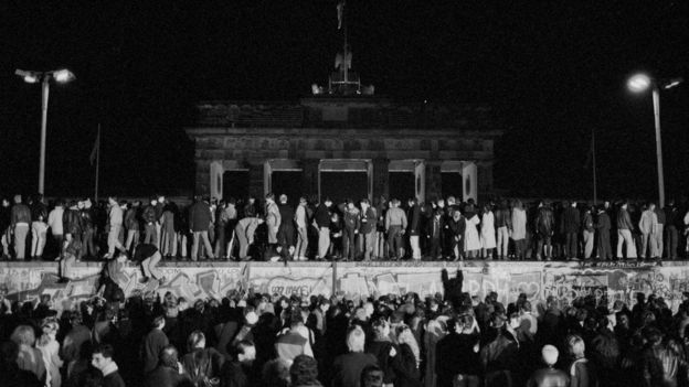 East and West German citizens celebrate as they climb the Berlin Wall at the Brandenburg Gate after the opening of the East German border was announced in Berlin, on 9 November, 1989