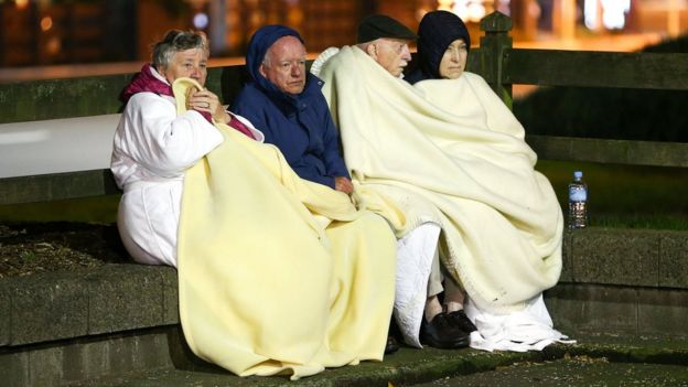 Four people sit on a low wall under blankets after the earthquake