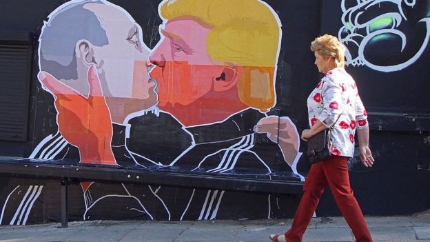 Una mujer pasa frente a un mural en el que Trump y Putin se besan