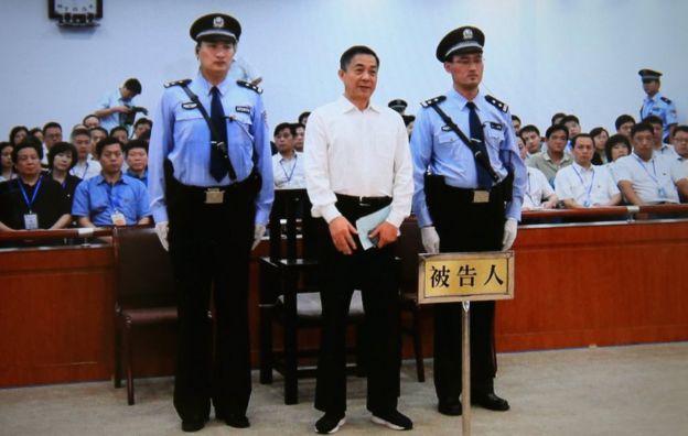 A screen shows the sentence of Chinese politician Bo Xilai (centre, flanked by security guards and with court attendees behind) on 22 September 2013 in Beijing, China.