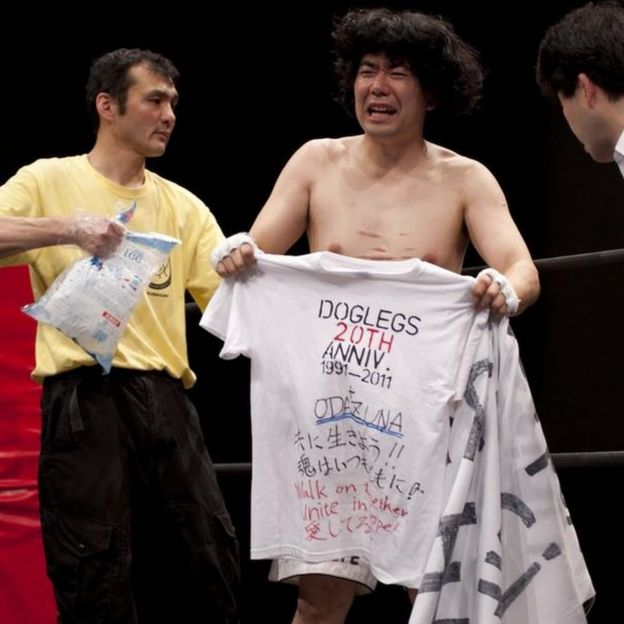 Nakajima holding up a shirt for the Dog Legs 20th anniversary