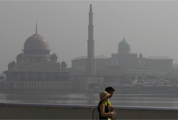 Tourists walk past Putrajaya's iconic buildings, from left to right, Putra Mosque and prime minister's office shrouded with haze in Putrajaya, Malaysia on Wednesday, 16 September 2015