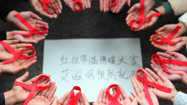 This picture taken on November 30, 2015 shows volunteers holding red ribbons above a piece of paper written in Chinese that reads ''Red ribbons bring warmth to everyone to prevent AIDS'