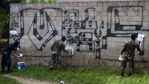 Policías borrando pintas alusivas a la Mara Salvatrucha en una pared de ladrillo de Quezaltepeque, una ciudad a 15 kilómetros de San Salvador.