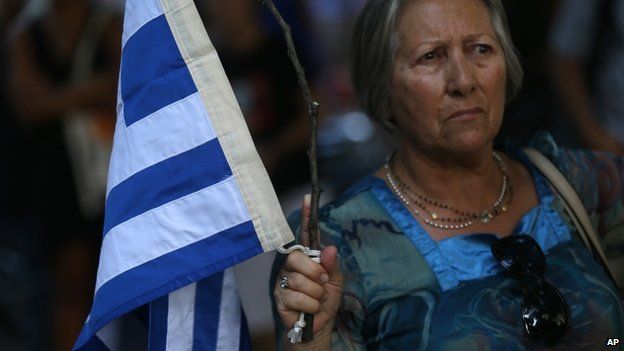 A woman holds a tree branch with a Greek flag tied on it during a rally in support to the Greek government