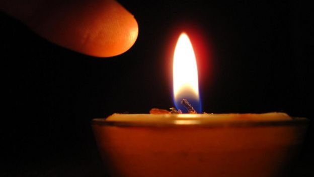 Una persona a punto de tocar la flama de una vela