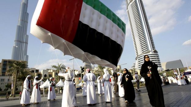 Жители несут государственный флаг перед самым высоким в мире небоскребом - башней Бурдж-Халифа - во время торжеств по случаю Национального дня ОАЭ (Дубай)