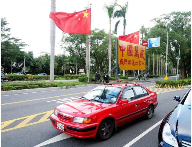A member of a pro-unification group drives a red car displaying China's national flags and a sign saying 