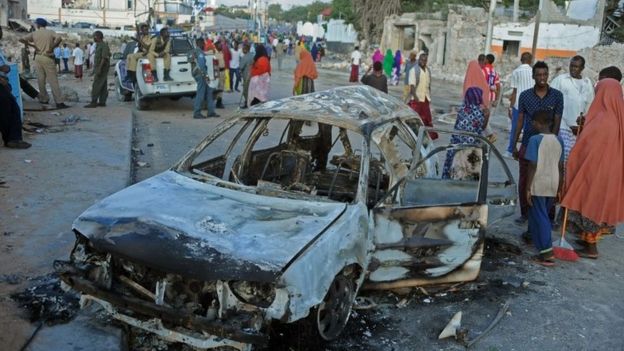 Somali civilians walk past a wreckage car after the attack on SYL hotel on February 26