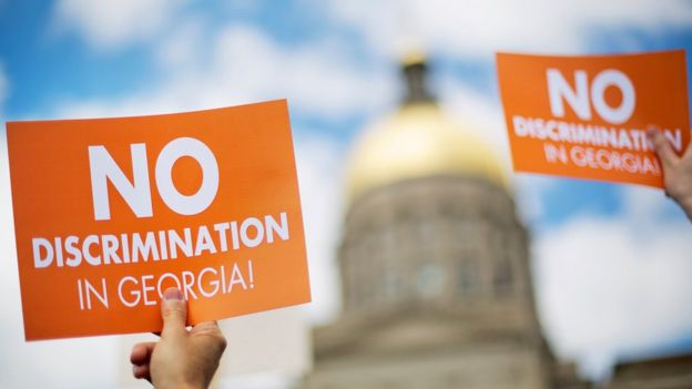 Protesters hold up signs as the dome of the Capitol stands in the background during a rally against a contentious 