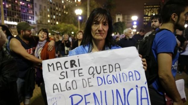 A woman holds a sign that reads in Spanish 