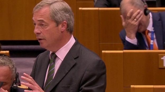 An EU commissioner reacts as UKIP leader Nigel Farage speaks