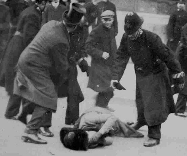 Woman lying on ground after benig injured, surrounded by policemen, 18 November 1910