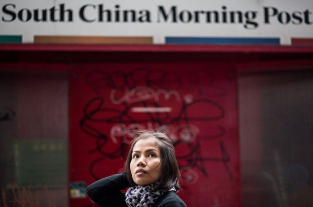 Woman walks past South China Morning Post sign