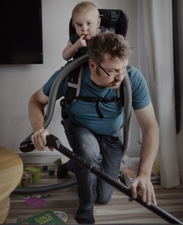 Man vacuuming with his son on his back