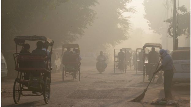 An Indian worker sweeps as smog envelops a street in the old quarter of Delhi on November 3, 2016.