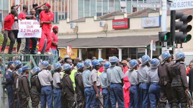 Zimbabwean police officers keep an eye on opposition party supporters as they prepare to march during a protest aimed at President Robert Mugabe in Harare, Zimbabwe, Thursday, March, 14, 2016