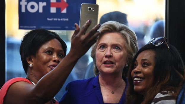 Hillary Clinton tomándose una selfie con dos votantes.