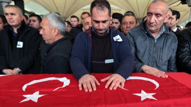 People stand by a coffin draped in a Turkish flag for a Turkish security agent killed in a suicide blast